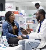 Professional black pharmacist providing expert medication advice to a female customer at the drugstore, explaining dosage and treatment options during a routine consultation service.