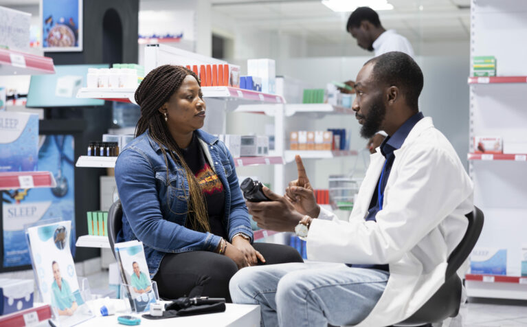 Professional black pharmacist providing expert medication advice to a female customer at the drugstore, explaining dosage and treatment options during a routine consultation service.
