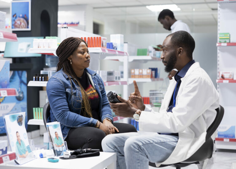 Professional black pharmacist providing expert medication advice to a female customer at the drugstore, explaining dosage and treatment options during a routine consultation service.